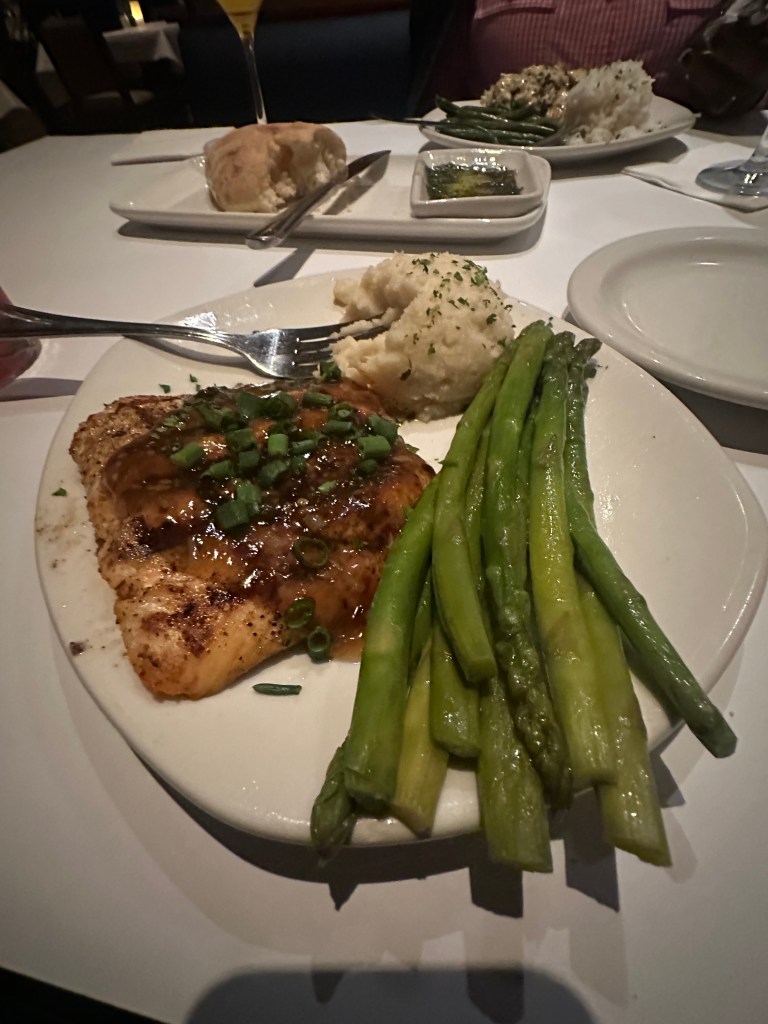 A plate featuring grilled fish topped with green onions, served with a side of mashed potatoes and steamed asparagus.